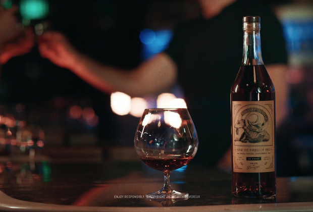 A bottle of Smith Devereux spirits with a vintage-style label next to a snifter glass filled with amber liquid