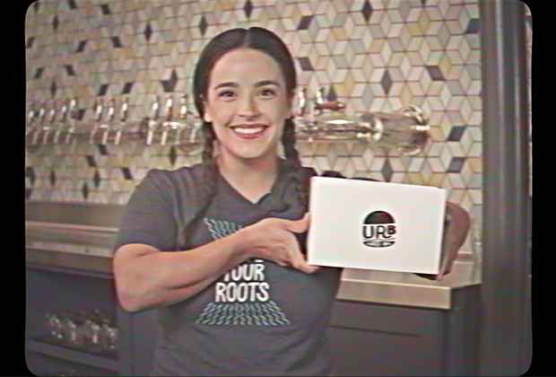A woman smiling as she holds up a box labeled Urban Roots.