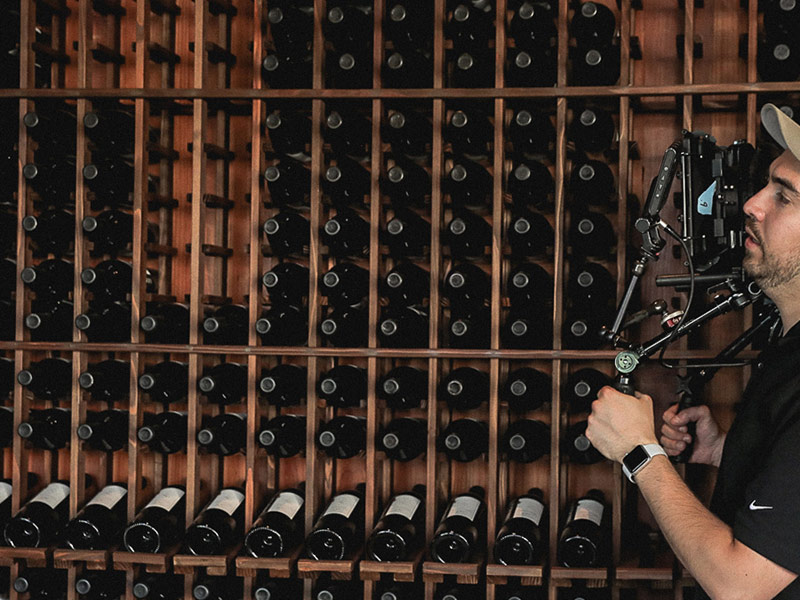 WineryHunt Case Study Still 2 Behind-the-scenes of Pour's crew member holding a camera rig, filming in front of a wine rack filled with numerous bottles of wine.