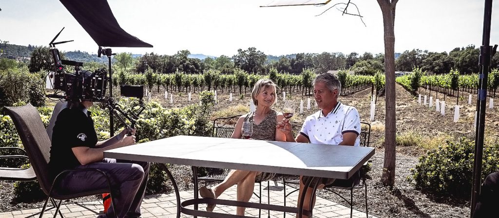 WineryHunt Case Study Still Vinsta Grape A camera crew is filming two people sitting at an outdoor table in a vineyard.