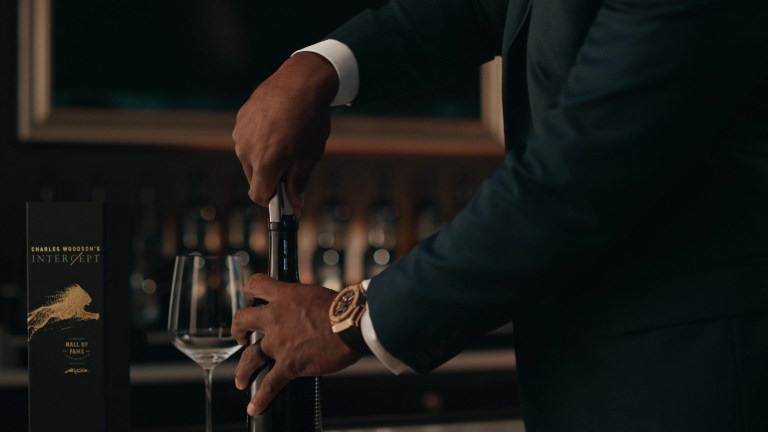 Person in a suit using a corkscrew to open a wine bottle labeled 'Charles Woodson's Intercept Hall of Fame.