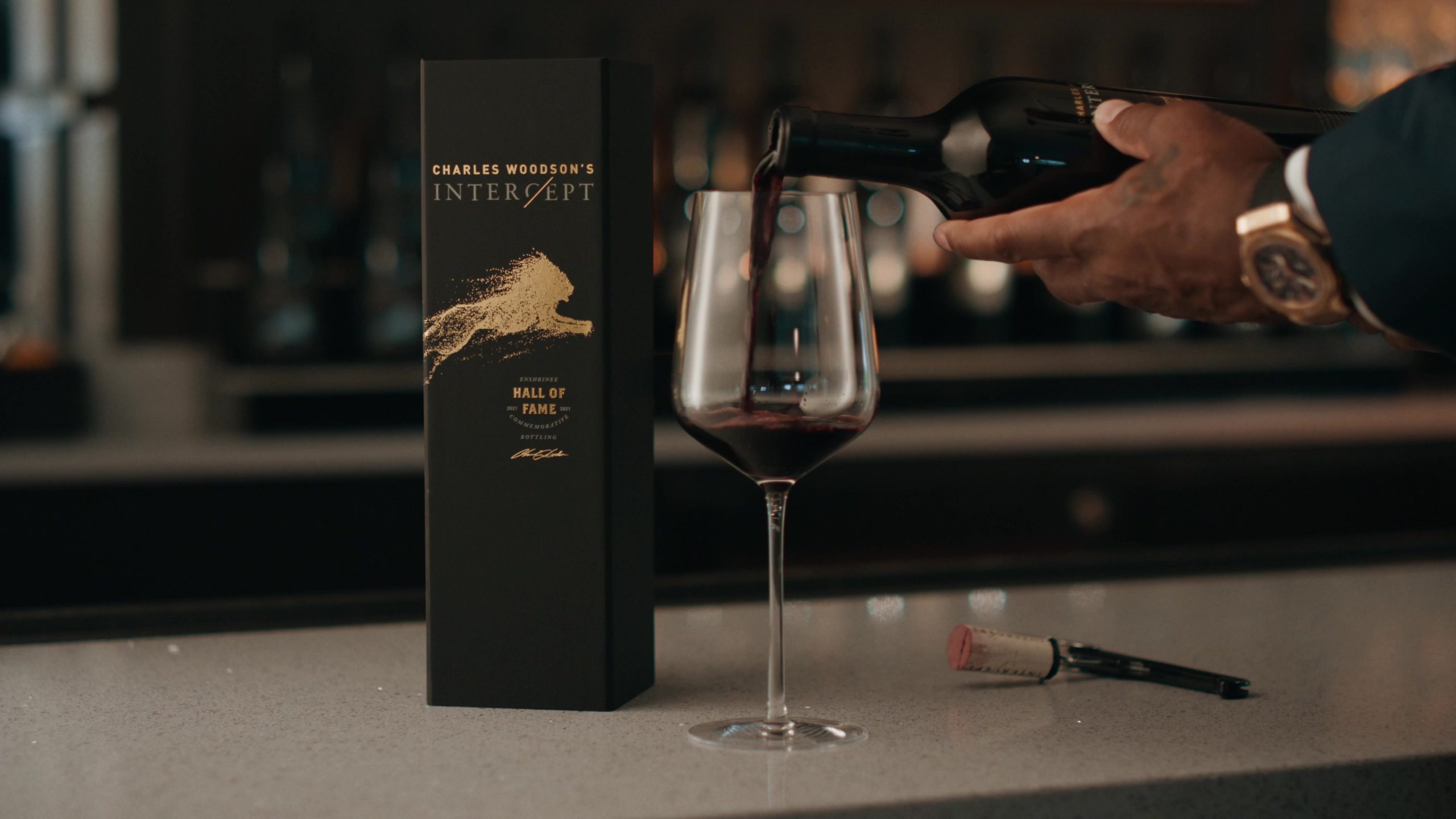 Person pouring red wine from a bottle labeled 'Charles Woodson's Intercept' into a wine glass.