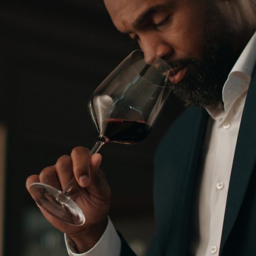Charles Woodson holding a wine glass by the stem and smelling the wine.