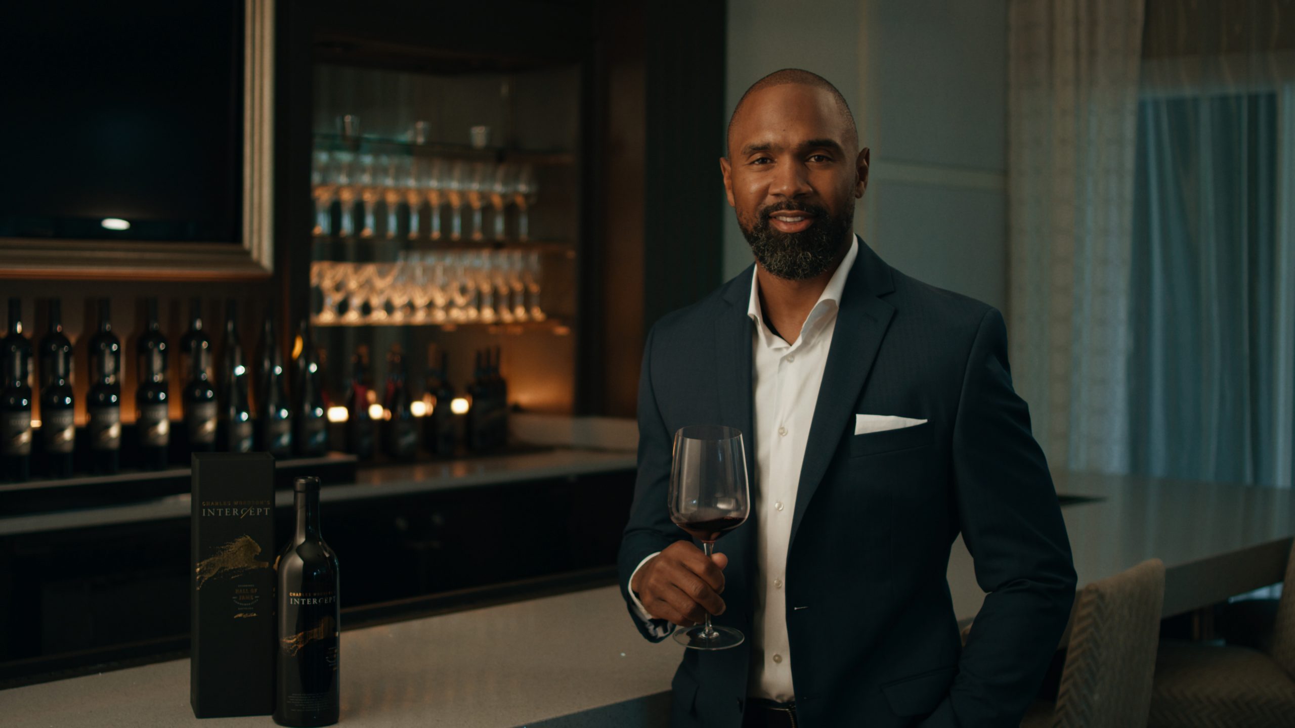 Charles Woodson in a suit holding a glass of wine in a dimly lit bar area.