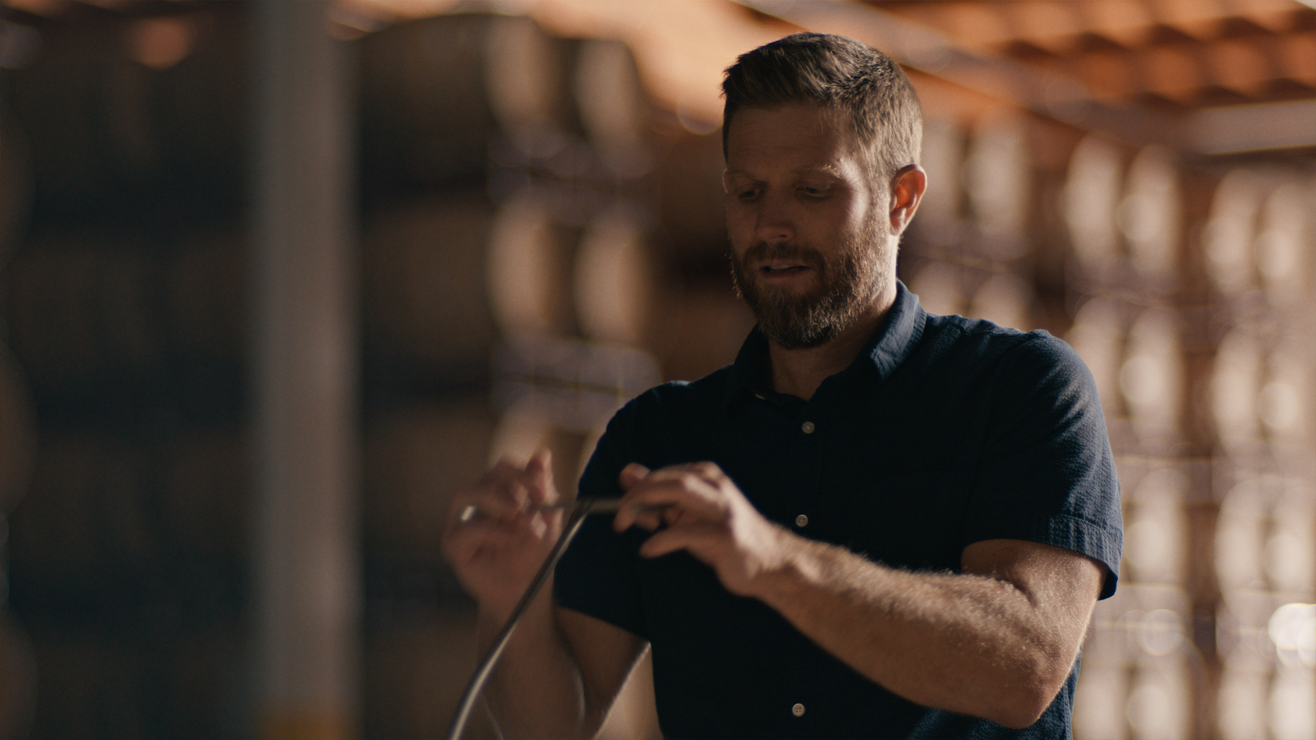 Person holding a tool in a storage area with wooden barrels in the background.