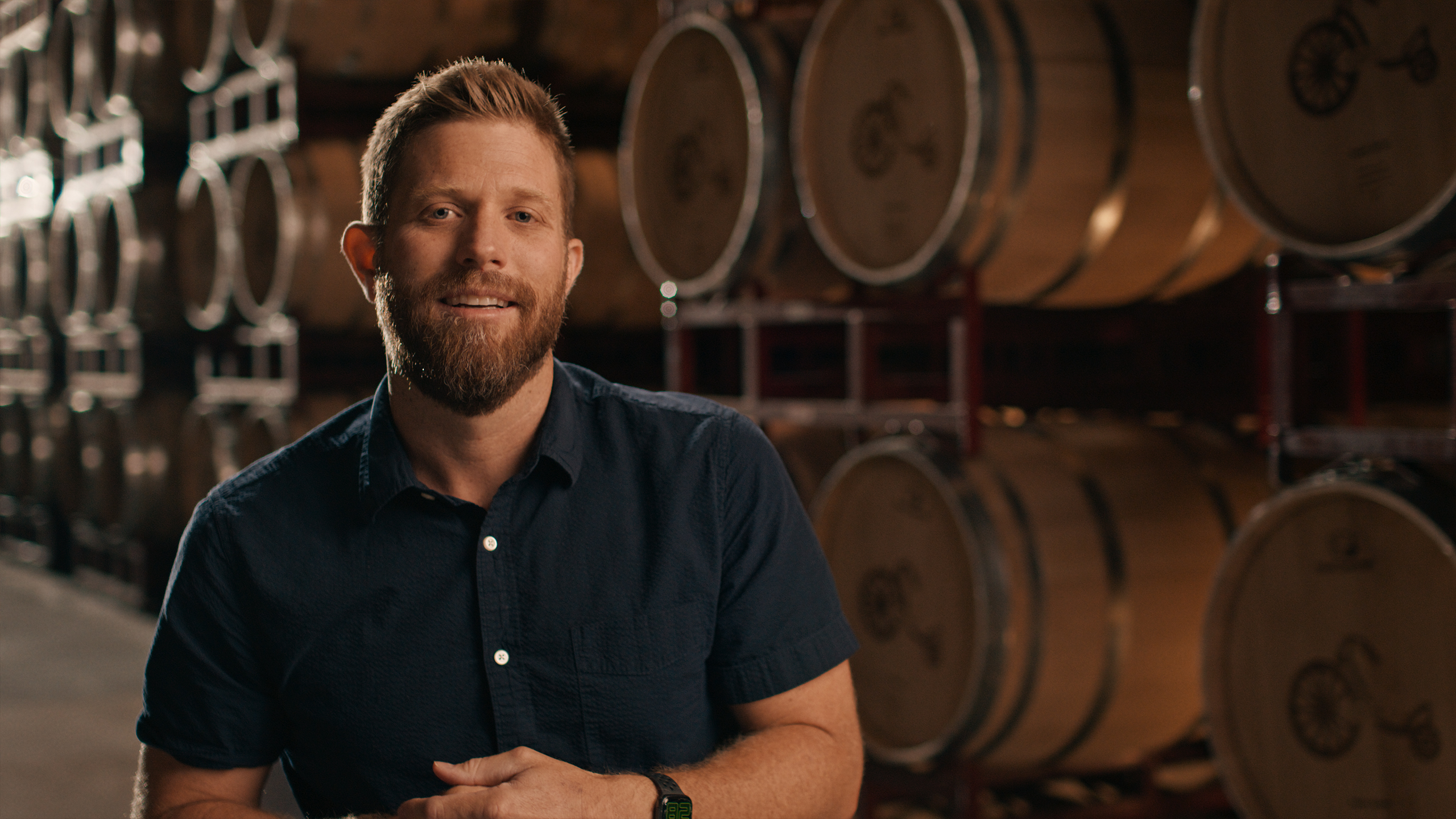 A man standing in a warehouse with rows of large wooden barrels.