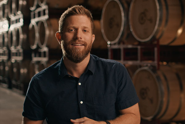 A man standing in a warehouse with rows of large wooden barrels.
