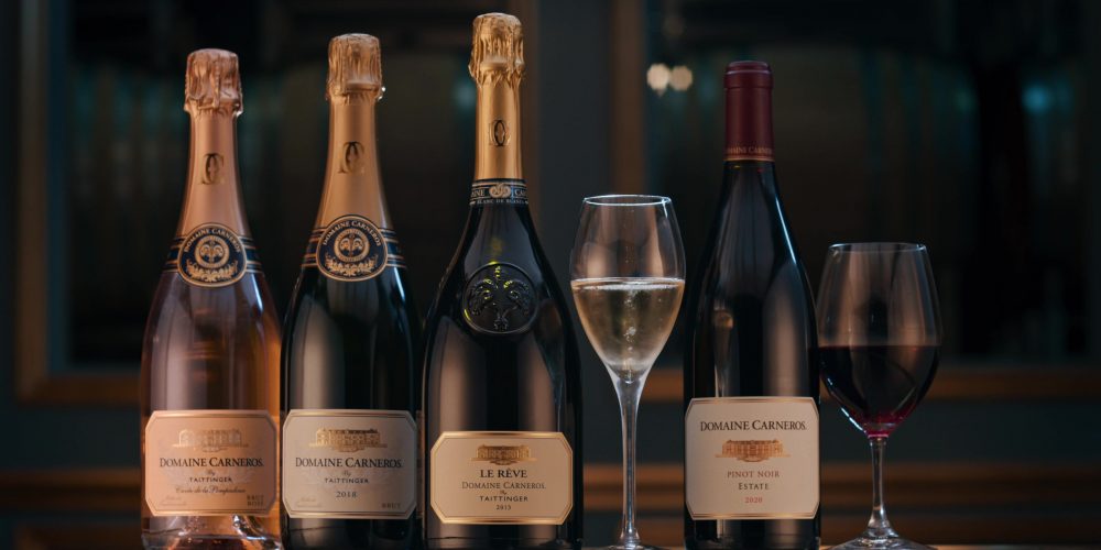 Four bottles of Domaine Carneros wine alongside two wine glasses.