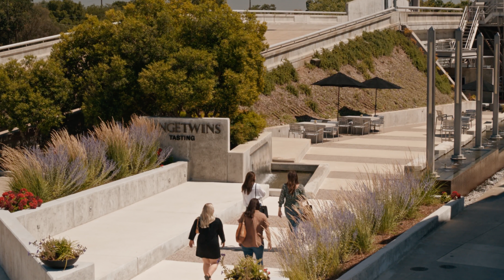 Four people walk towards the 'LangeTwins Tasting' area, surrounded by ornamental grasses. Tables with umbrellas are set up in the background, creating an inviting outdoor space.